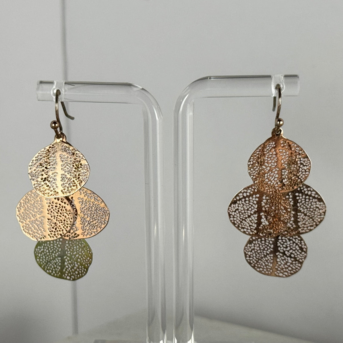 Pair of gold earrings on clear stands against a gray background