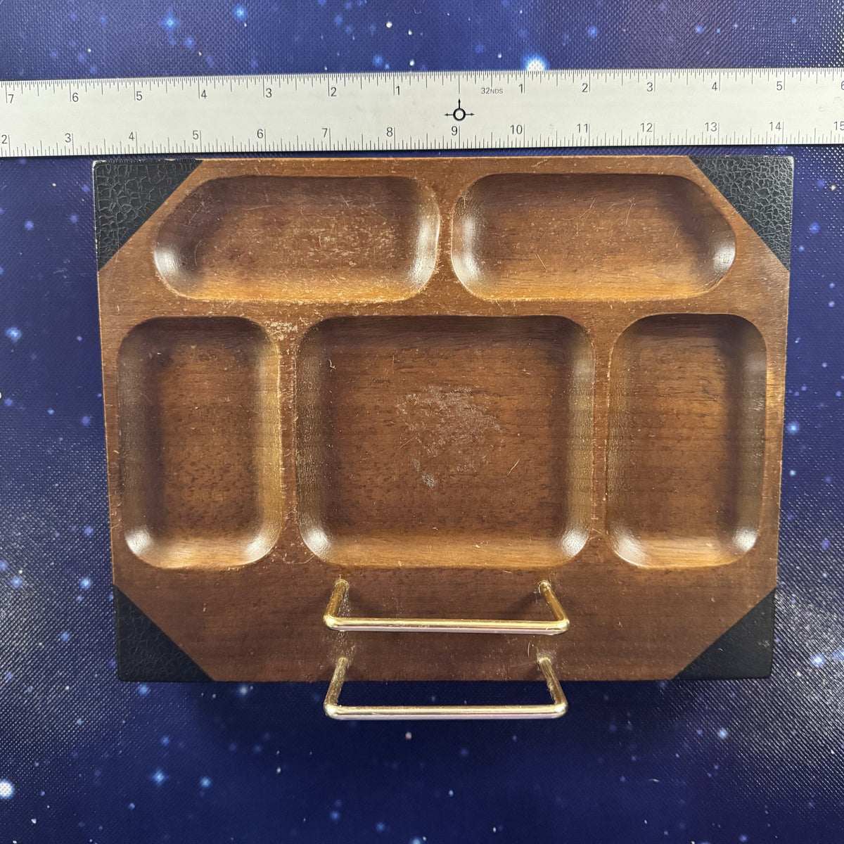 A wooden compartment tray with a gold metal handle, shown on a blue starry background next to a ruler for scale.