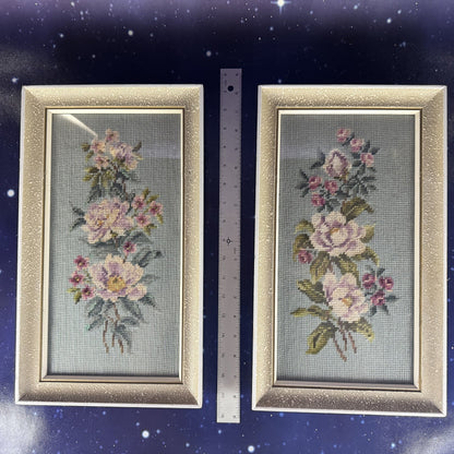 Two framed floral cross-stitch pieces on a dark blue background with a ruler for scale.