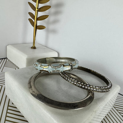 Three silver rings on a marble surface with a decorative plant in the background.