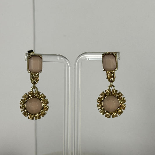 A pair of gold-tone drop earrings with rectangular blush pink stones at the top and round blush pink stones in ornate circular settings below, displayed on clear acrylic stands against a light gray background.