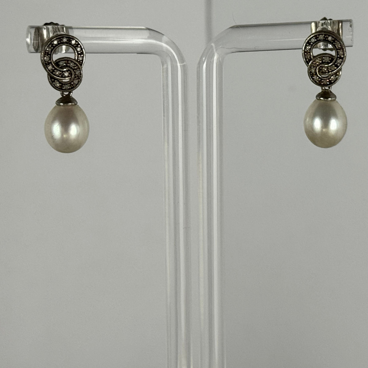 Pair of pearl earrings on a clear stand against a gray background
