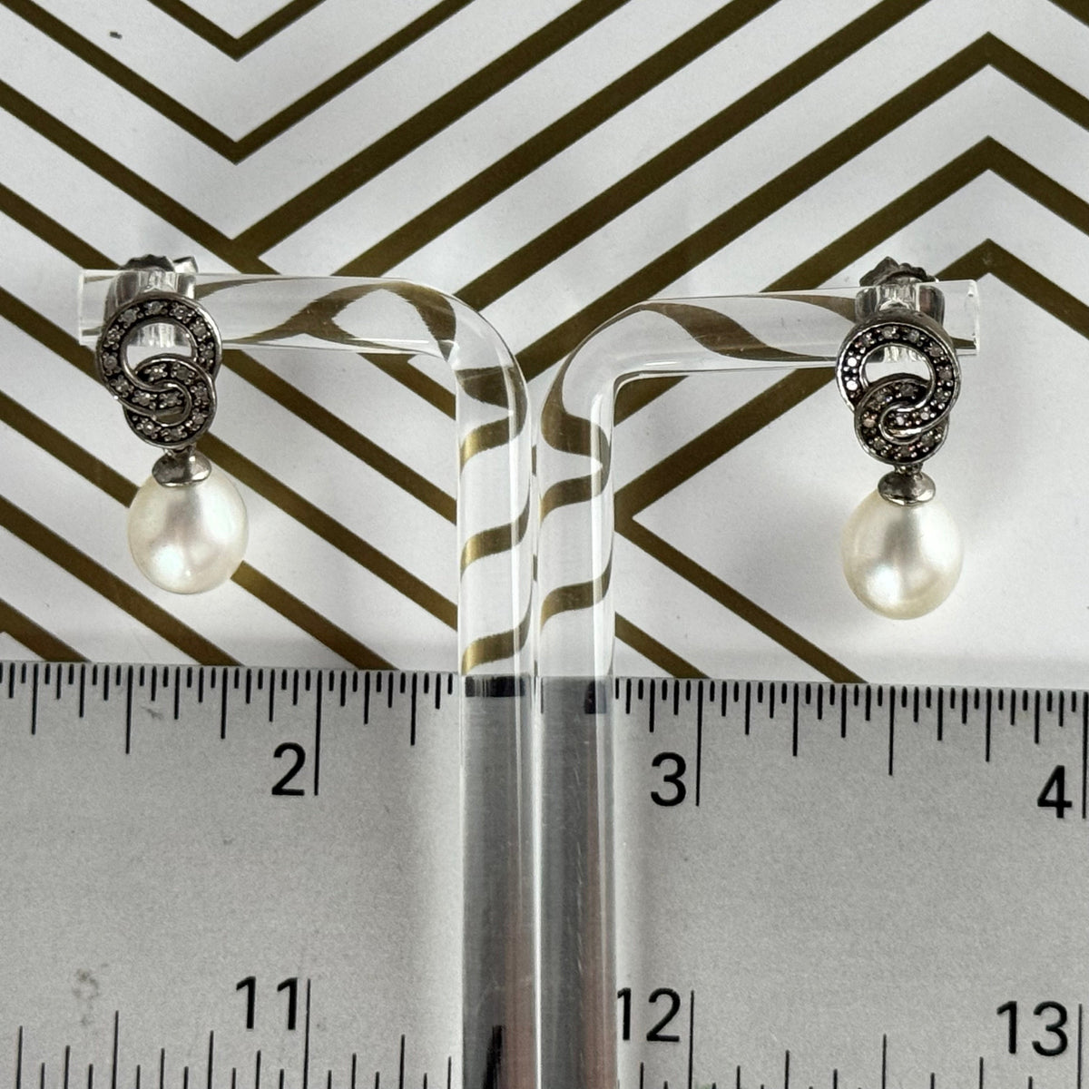 Pair of earrings on clear stands with a ruler for scale against a striped background