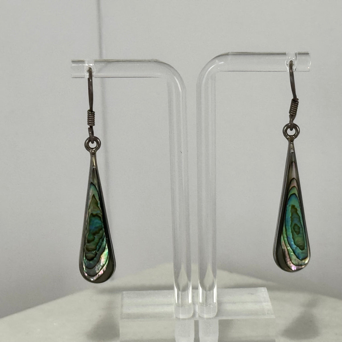 Teardrop-shaped earrings with green and black pattern on a clear stand against a white background