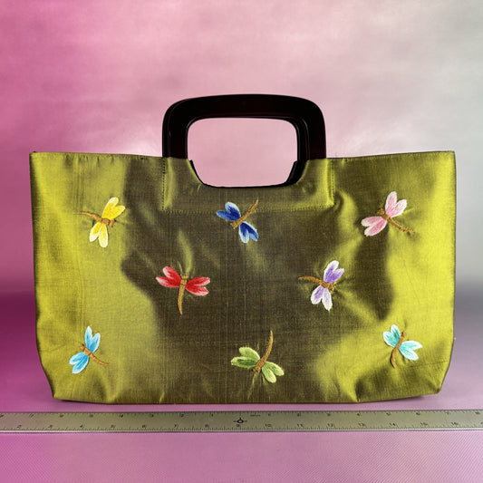 Green bag with colorful dragonfly designs on a pink gradient background