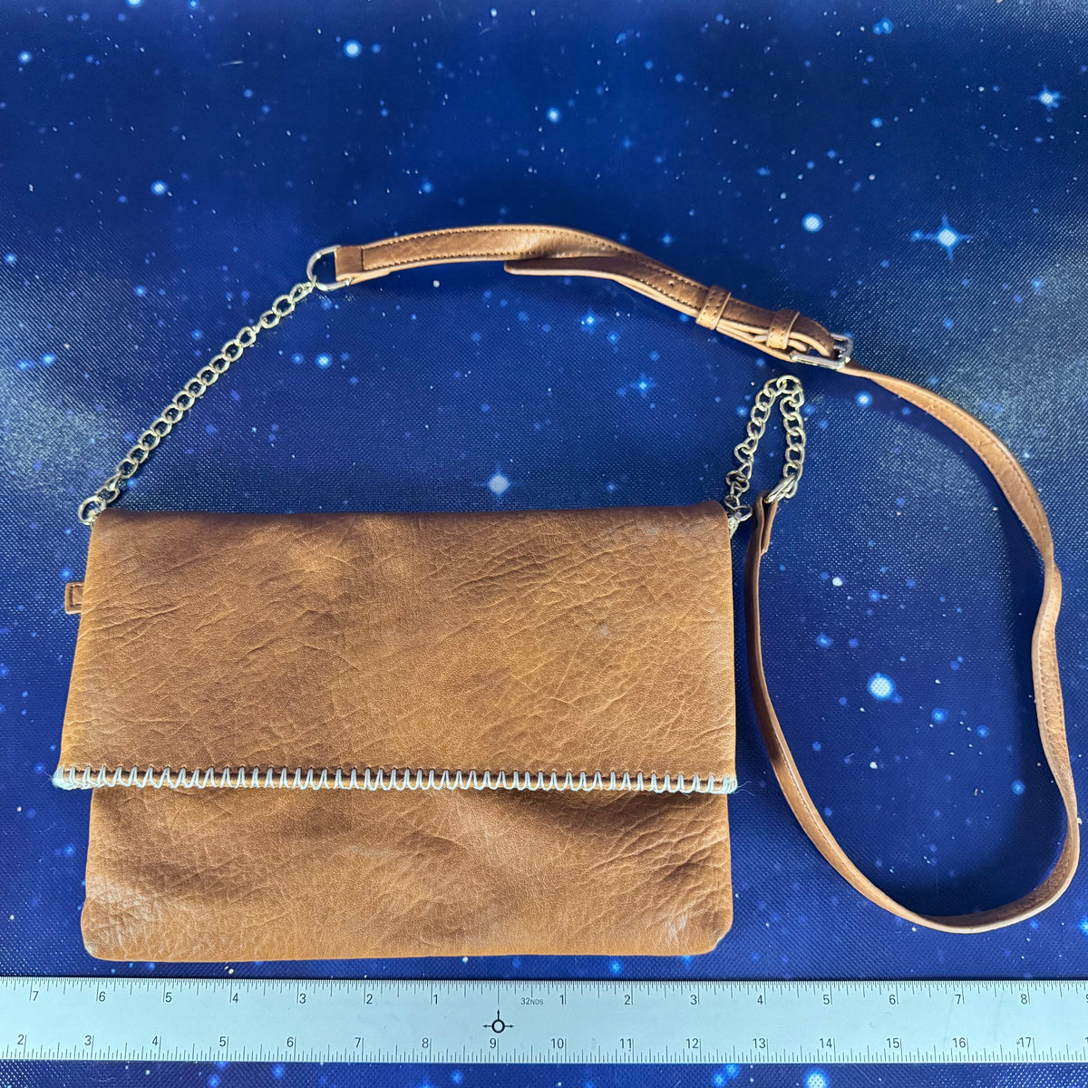 Brown leather handbag with chain strap on a blue starry background