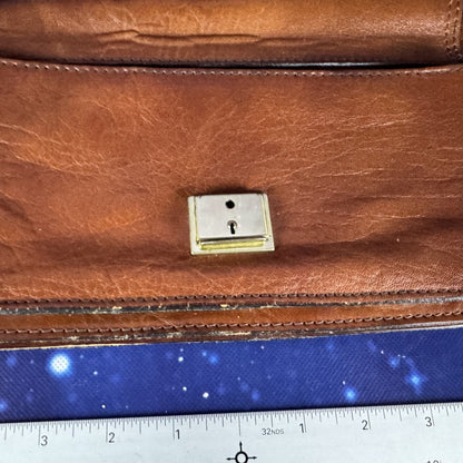 Brown leather bag with a gold clasp on a blue fabric background with a ruler at the bottom.