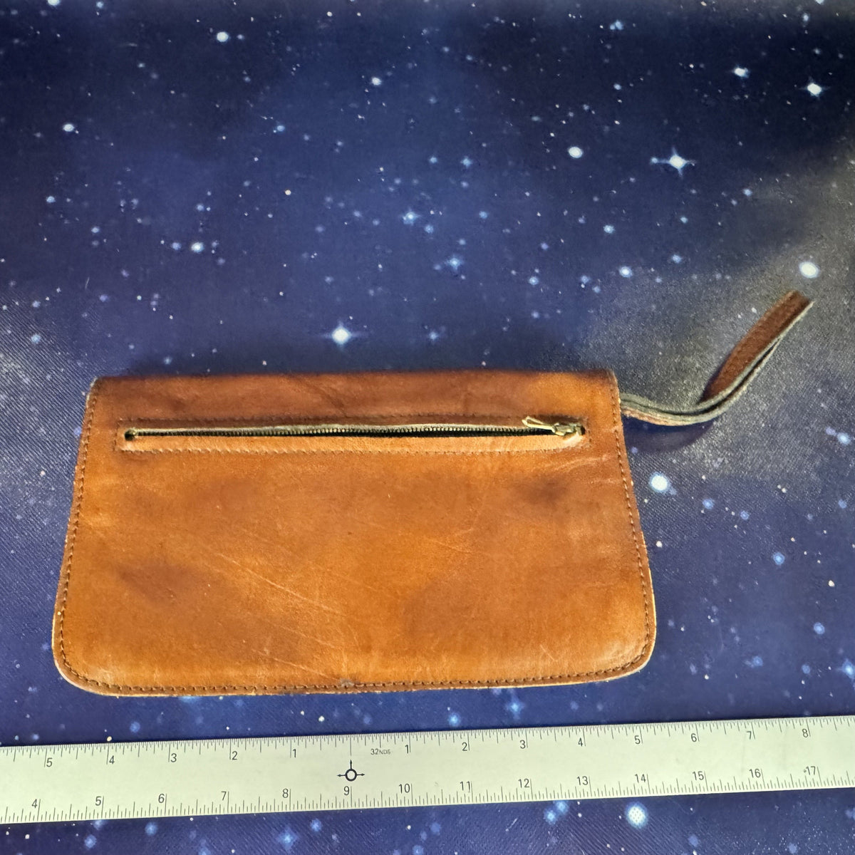 Brown leather clutch with gold zipper on a starry background