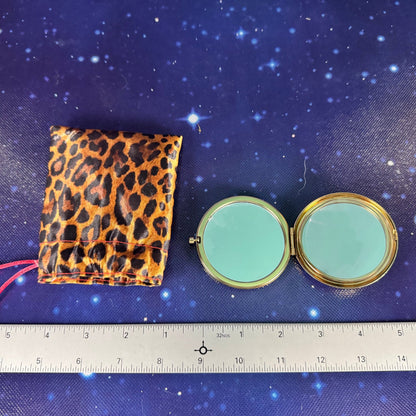 Compact mirror and leopard print pouch on a blue fabric background with a ruler above.
